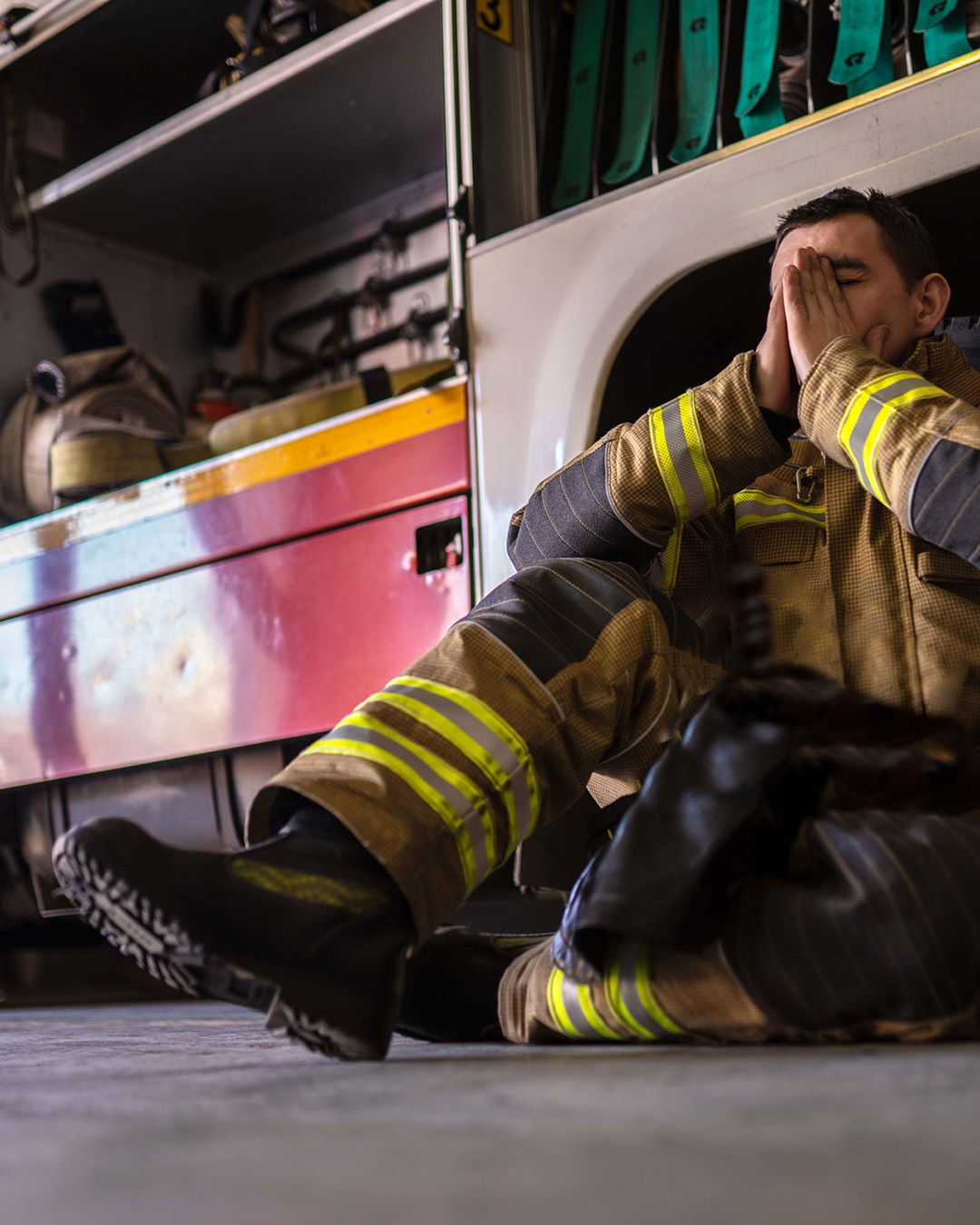Firefighter sitting by firetruck covering face with hands